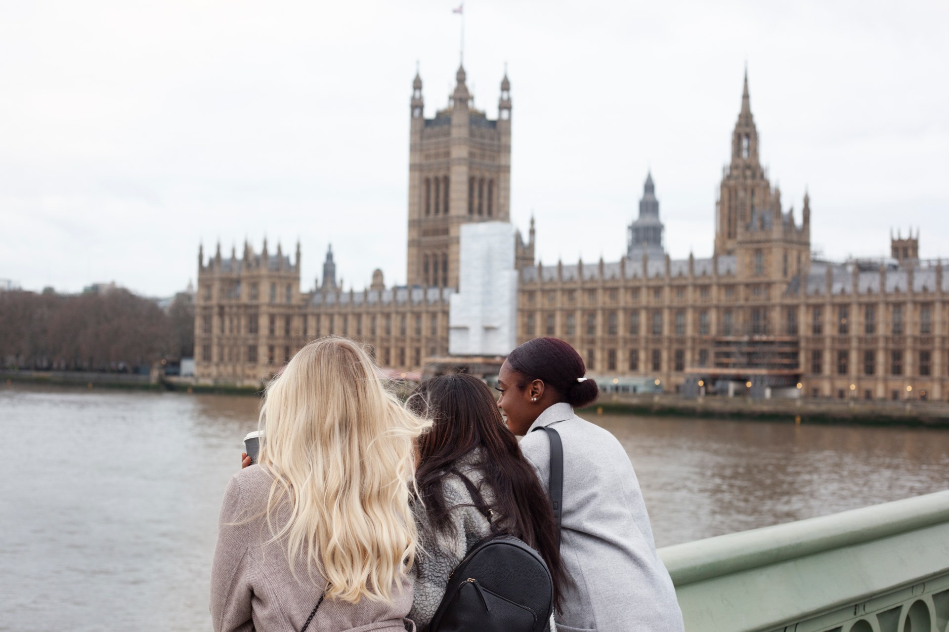 Three young women by the Thames in London, with the Palace of Westminster behind them